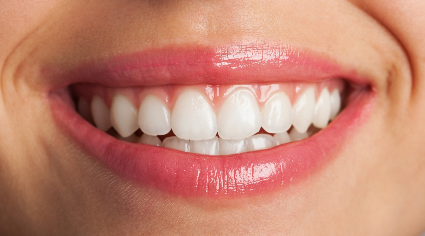 Close-up of a person's healthy, white smile with glossy pink lips.