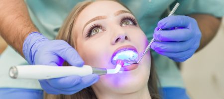 Dentist uses UV light to cure dental bonding on a woman's tooth.